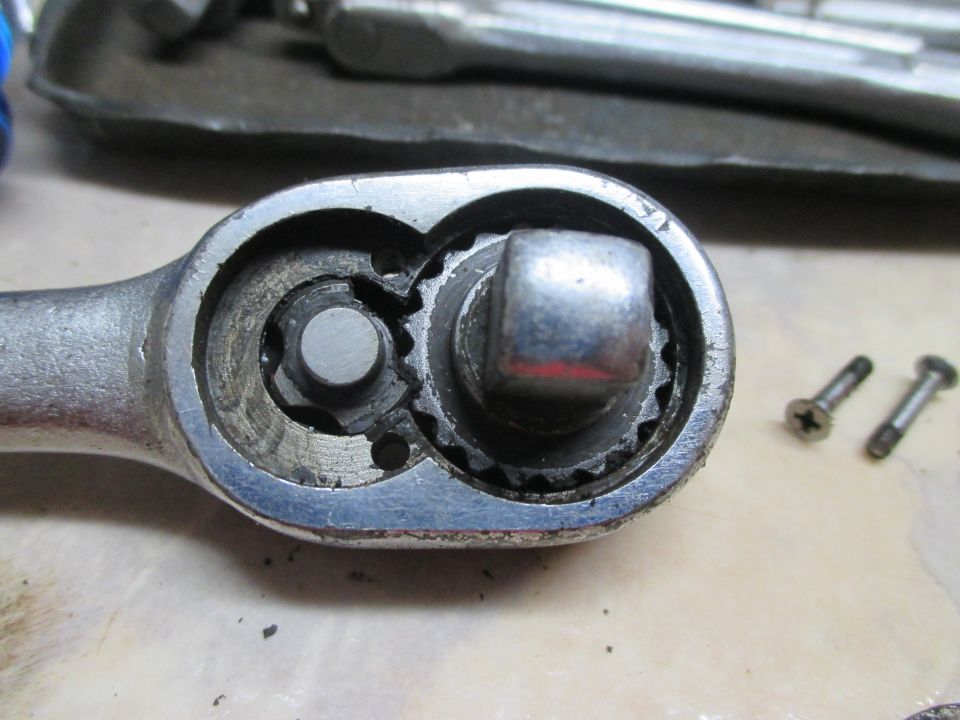 Close-up of a ratchet wrench head showing the internal gears and a square drive. Two small screws are visible to the right