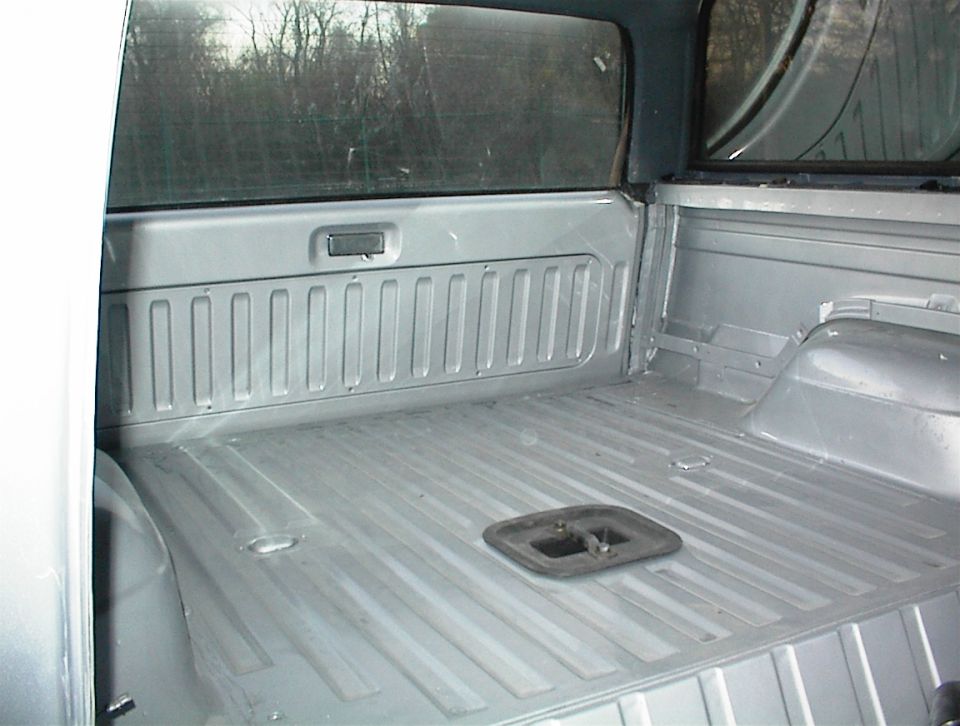 Empty silver truck bed with ribbed floor and sides. A black tie-down anchor is visible