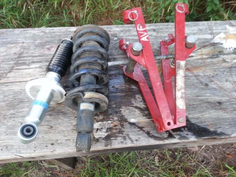 2006 Nissan Titan - A pair of vehicle struts and a red spring compressor tool are laid out on a weathered wooden surface, with grass in the background.