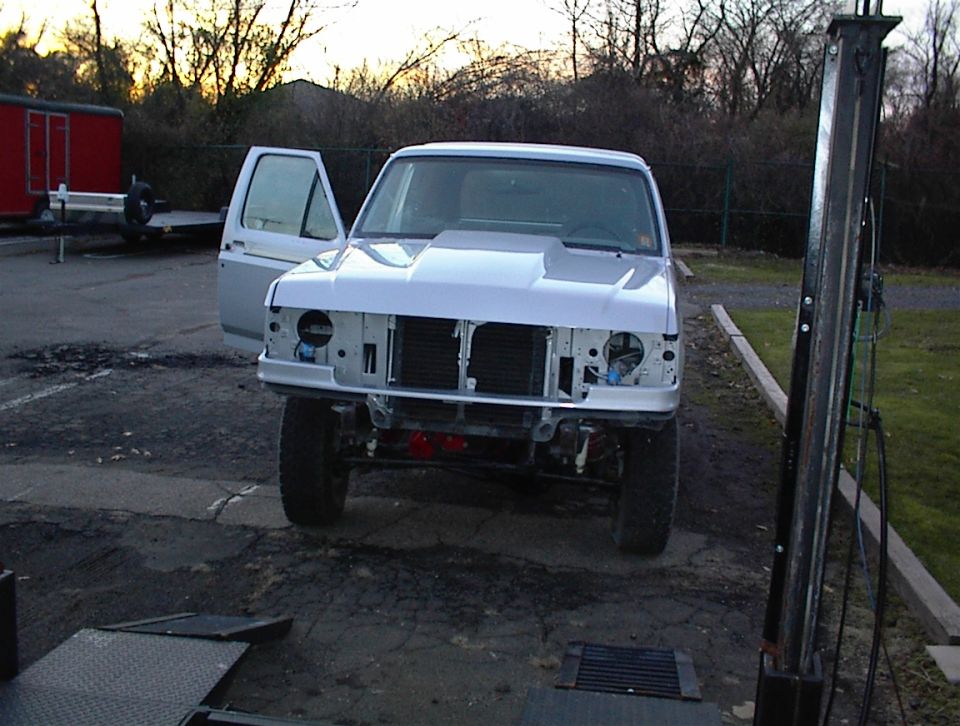 White Ford Bronco with hood scoop, open driver door, and missing grille, parked outdoors