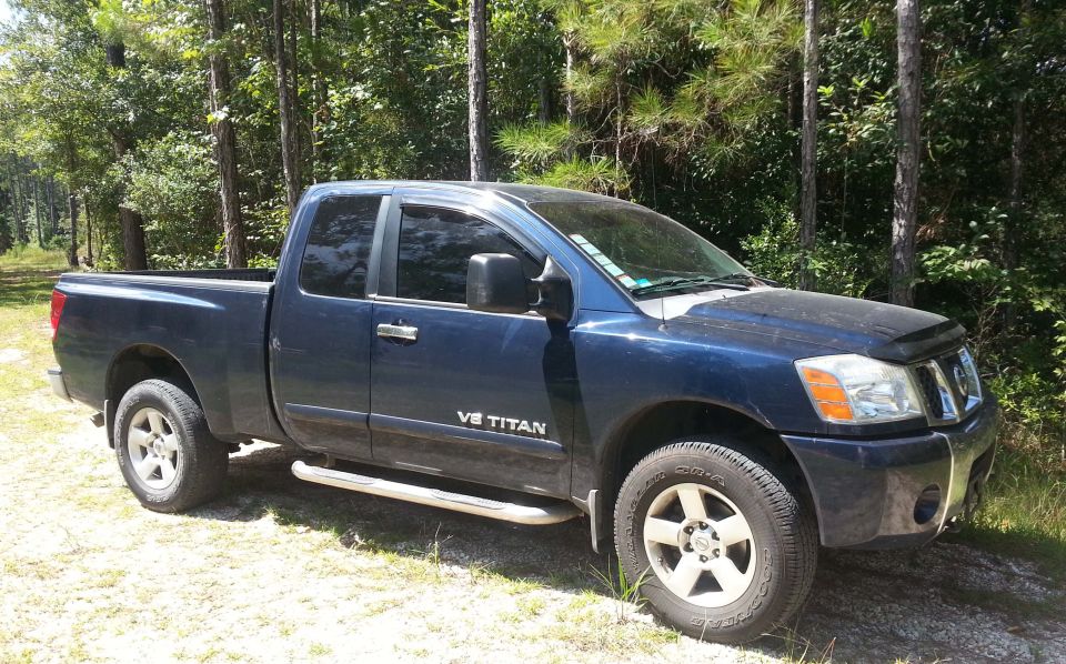 2006 Nissan Titan pickup truck, dark blue, parked on dirt with trees in background