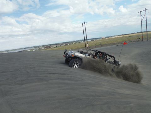 2005 Jeep Wrangler - A silver Jeep Wrangler navigates a sandy dune, kicking up a cloud of dust.