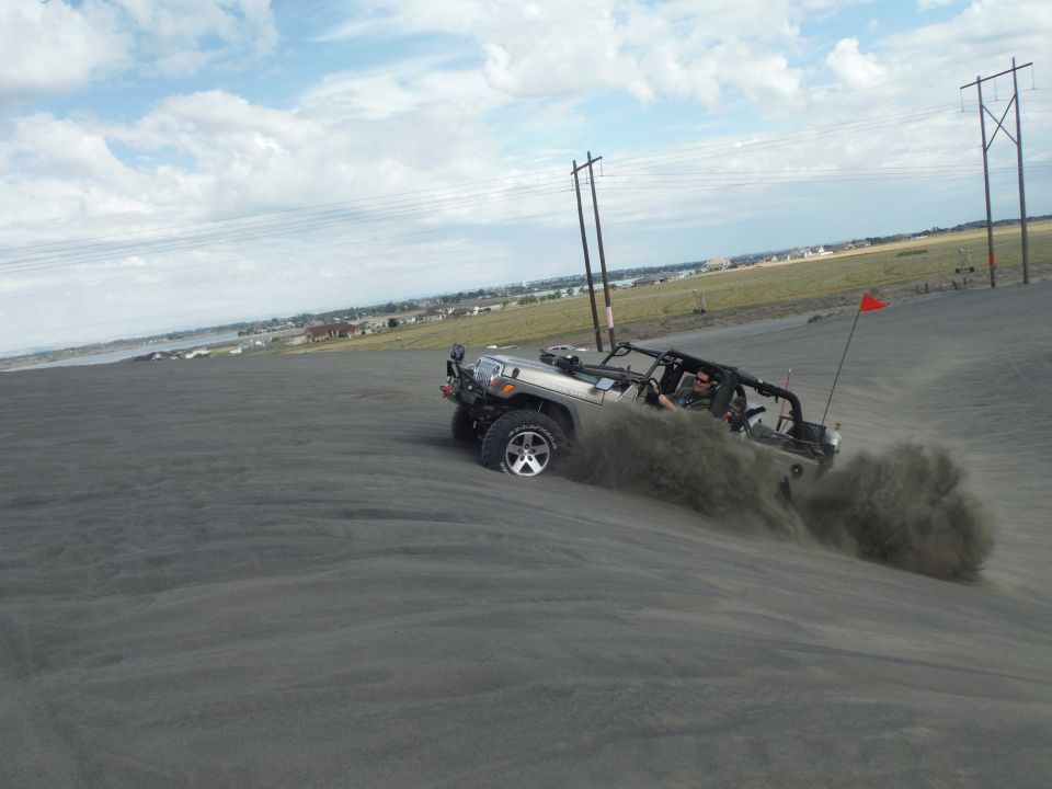 Silver Jeep Wrangler kicking up sand on a dune