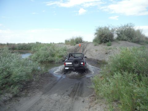 2005 Jeep Wrangler - 2005 Jeep Wrangler navigates a water obstacle on a dirt path, kicking up spray.