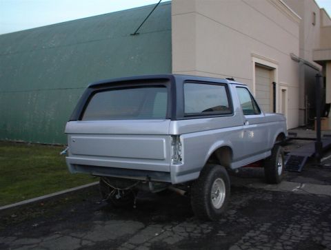 1990 Ford Bronco - Rear view of a silver 1990 Ford Bronco with a black top, parked outdoors.