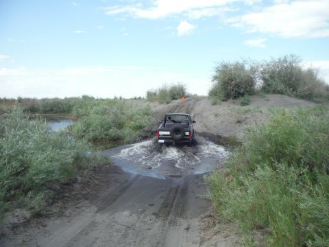 2005 Jeep Wrangler - Jeep Wrangler navigates a water obstacle on a dirt trail surrounded by vegetation.
