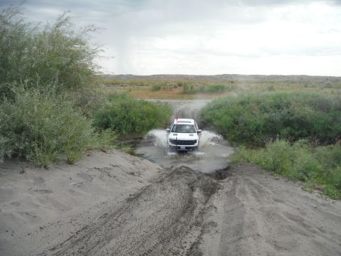 2005 Jeep Wrangler - A white SUV navigates a water crossing on a dusty trail under an overcast sky.