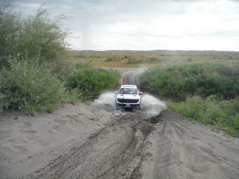 2005 Jeep Wrangler - A white SUV navigates a muddy track, kicking up water as it drives through a shallow puddle.