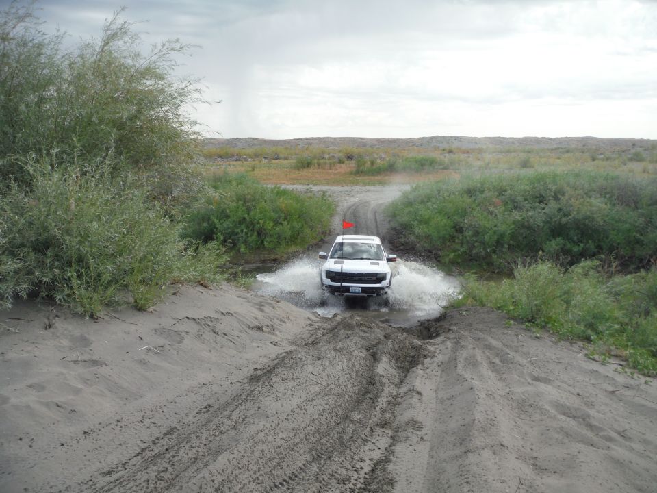 White SUV driving through water on a dirt road with vegetation