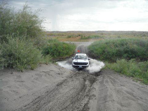 2005 Jeep Wrangler - A white SUV navigates a muddy obstacle on an off-road trail under an overcast sky.