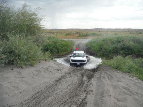 2005 Jeep Wrangler - A white SUV navigates a challenging off-road path, kicking up water and mud.
