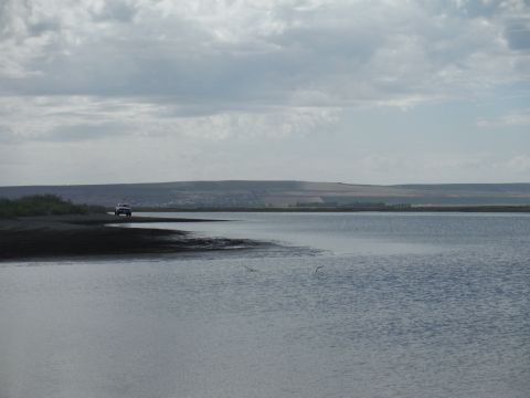2005 Jeep Wrangler - A lone SUV is parked on the edge of a dark shore, with a wide expanse of water stretching out before it under a cloudy sky.