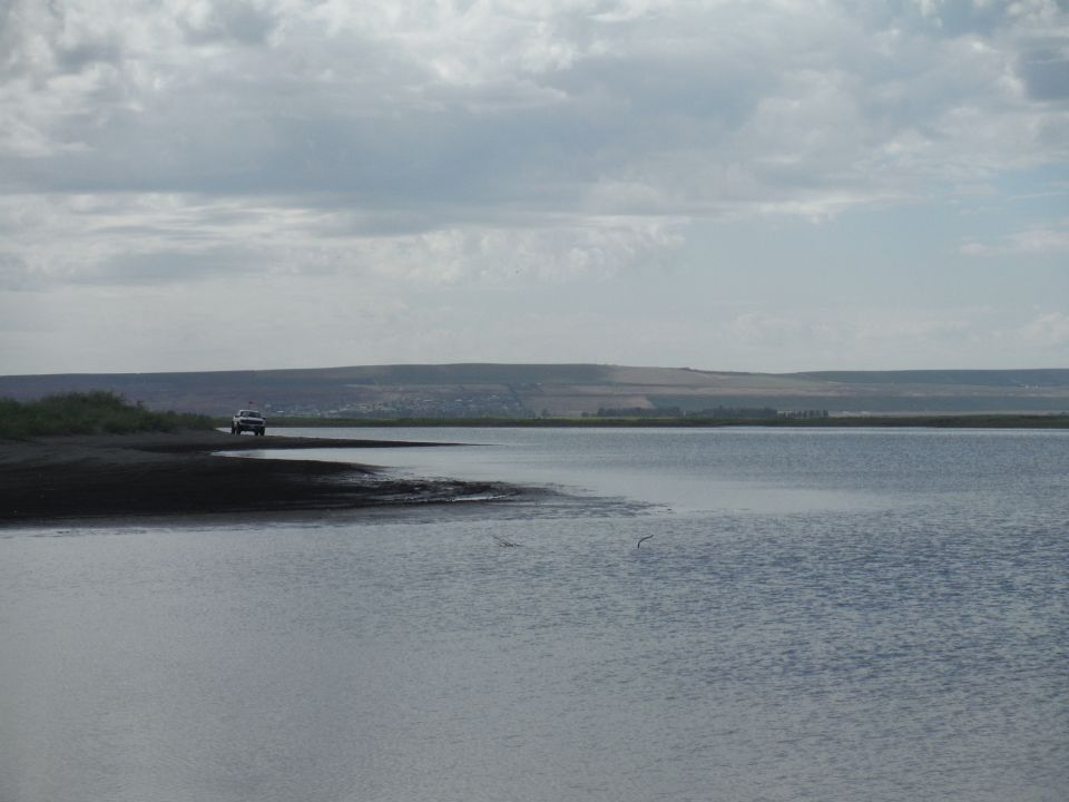SUV parked on a dark shore next to a large body of water under a cloudy sky