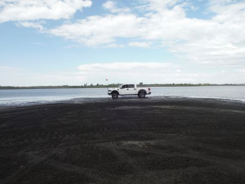 2005 Jeep Wrangler - A white pickup truck is parked on a dark sandy area next to a large body of water.