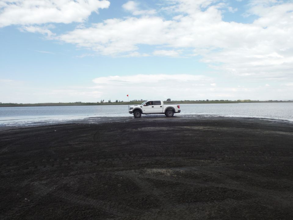 White pickup truck parked on dark sand near a body of water under a cloudy sky
