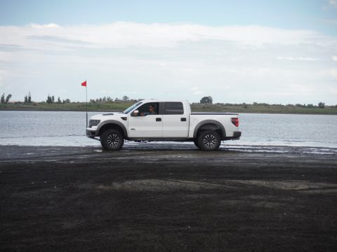 2005 Jeep Wrangler - A white pickup truck drives along the edge of the water on a sandy shore under a cloudy sky.