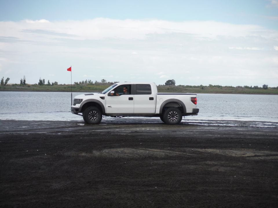 White pickup truck driving on a sandy beach next to water