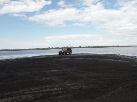 2005 Jeep Wrangler - A Jeep Wrangler drives along a dark sandy shore next to a body of water under a cloudy sky.