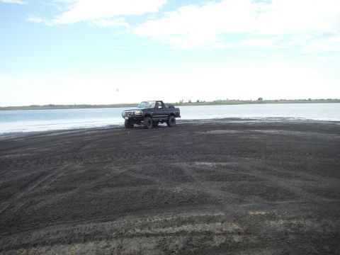 2005 Jeep Wrangler - A black Ford Bronco is seen driving on a dark, sandy shore with a calm body of water in the background under a cloudy sky.