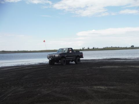 2005 Jeep Wrangler - A black Ford Bronco is driven on a sandy shore with a body of water in the background under a cloudy sky.