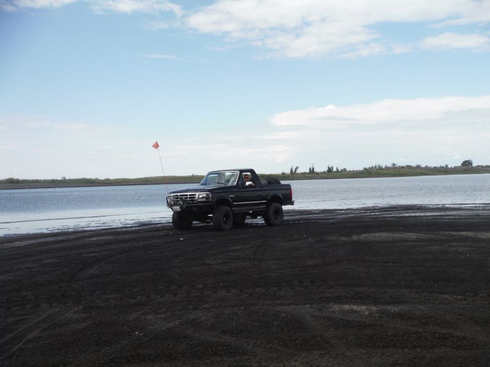Black Ford Bronco driving on a sandy beach next to a body of water