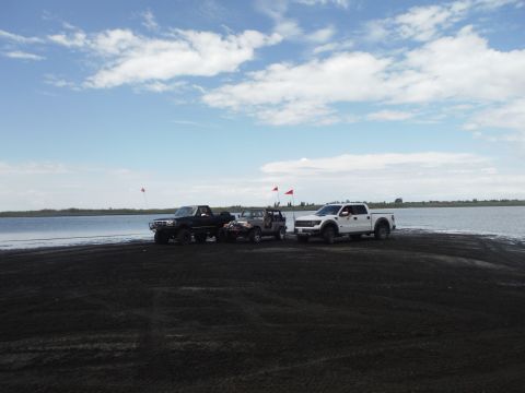 2005 Jeep Wrangler - Three off-road vehicles are parked on a sandy area next to a large body of water on a partly cloudy day.