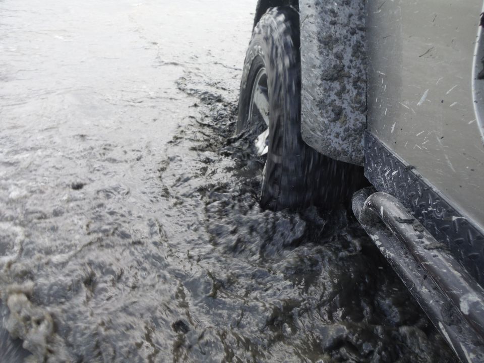 Silver Jeep Wrangler side view, tire in mud, side step visible