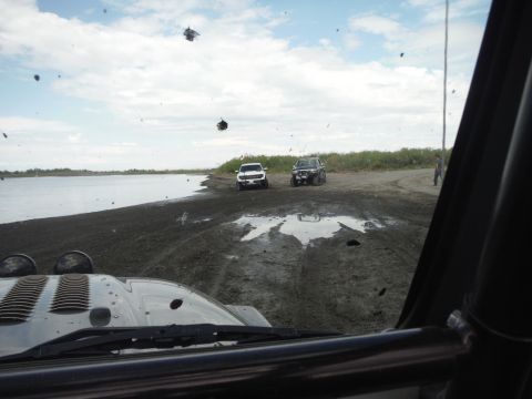 2005 Jeep Wrangler - Two off-road vehicles are parked on a muddy bank next to a large body of water under a cloudy sky.