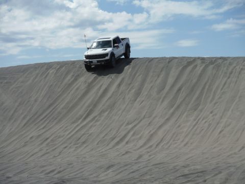 2005 Jeep Wrangler - A white pickup truck is positioned on the crest of a sand dune under a partly cloudy sky.