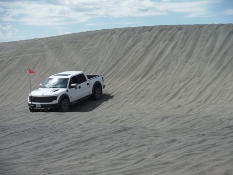 2005 Jeep Wrangler - A white Ford F-150 Raptor navigates a sandy terrain under a cloudy sky.