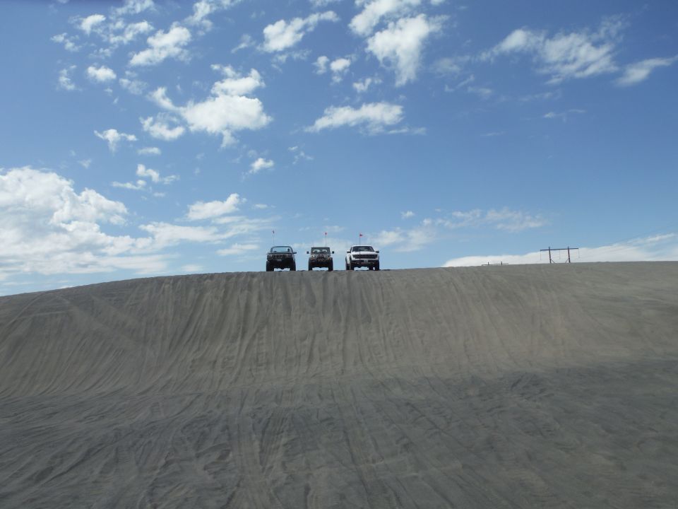 Three SUVs parked on top of a sand dune under a blue sky with scattered clouds