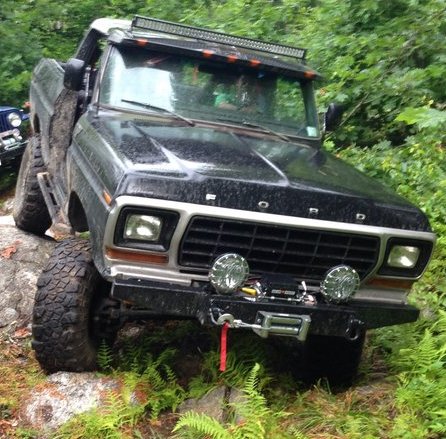 1979 Ford Bronco - A black Ford Bronco navigates a rocky, wooded path, with another vehicle visible in the background.