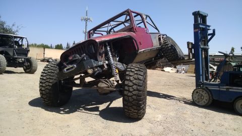 1985 Jeep CJ7 - This heavily modified Jeep features a custom roll cage and oversized tires, with a forklift assisting in its movement.