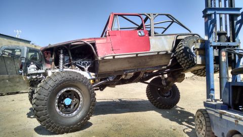 1985 Jeep CJ7 - Customized 1985 Jeep CJ7 undergoing modification, lifted by a forklift in an outdoor lot.