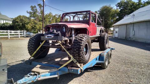 1985 Jeep CJ7 - This modified 1985 Jeep CJ7, equipped with oversized tires and a roll cage, is secured to a trailer for transport.