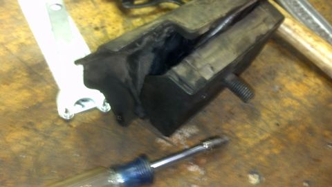 1995 Ford Bronco - A heavily worn rubber mount with a metal bracket and bolt is shown on a wooden surface.