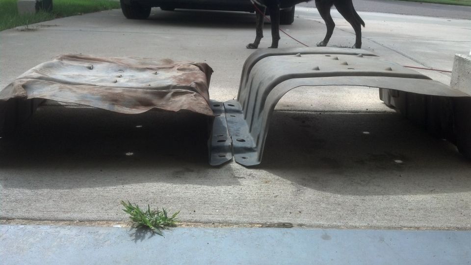 Two fuel tanks, one rusty metal and one black plastic, sit on a concrete driveway