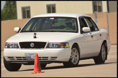 2000 Mercury Grand Marquis - White 2000 Mercury Grand Marquis sedan with a driver wearing a helmet, seen on a track with an orange cone.