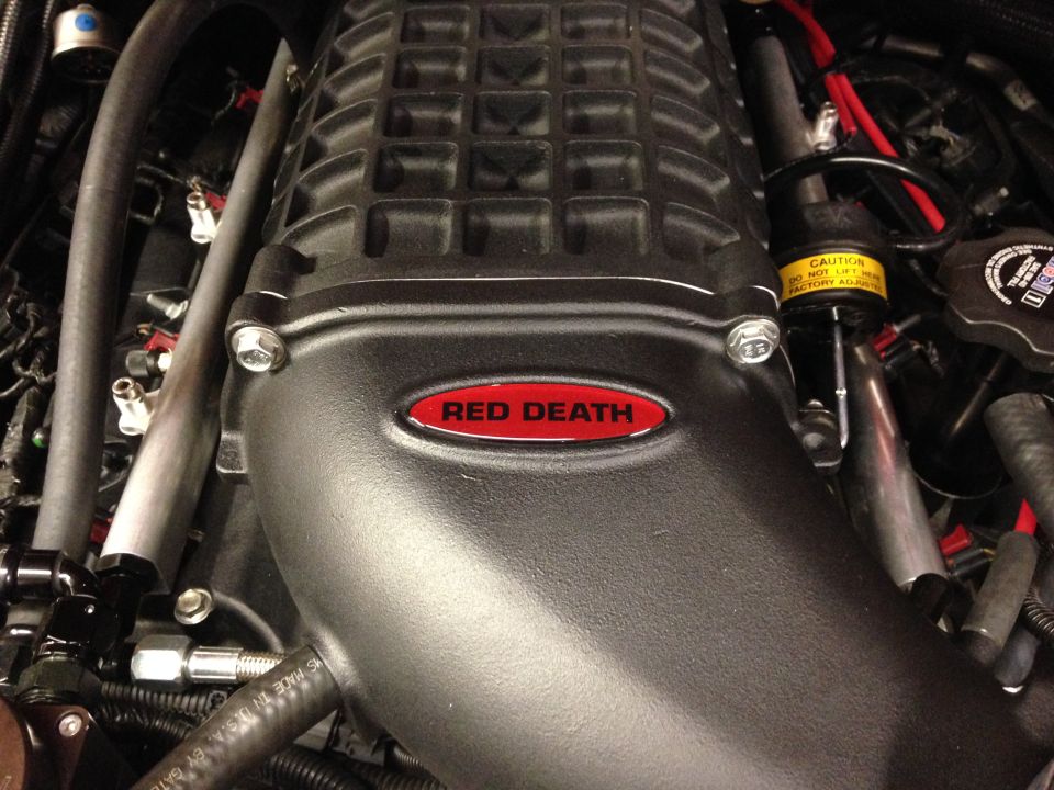 Close-up of a black supercharger with a red "Red Death" emblem. Some hoses and engine components are visible
