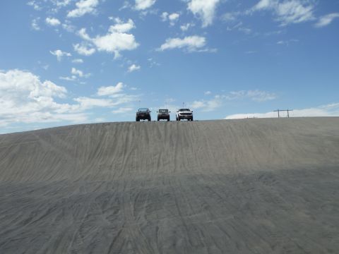2005 Jeep Wrangler - Three SUVs are seen driving on a sand dune under a bright blue sky with scattered clouds.