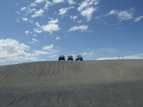 2005 Jeep Wrangler - Three SUVs are lined up on a sand dune against a bright blue sky with scattered clouds.