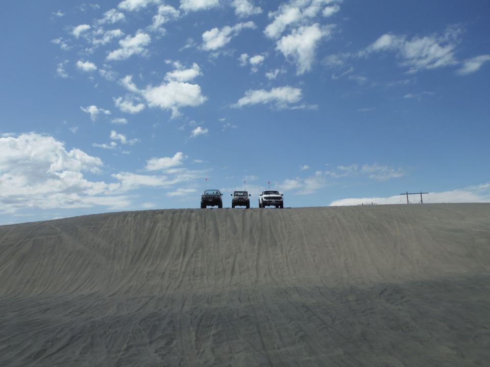 Three SUVs parked on top of a sand dune under a cloudy blue sky