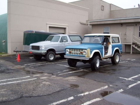 1969 Ford Bronco - A blue first-generation Ford Bronco is parked next to a silver pickup truck.