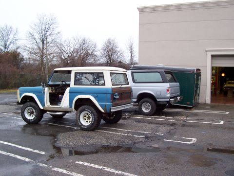 1969 Ford Bronco - Two Ford Broncos and a trailer are parked in a lot on a cloudy day.