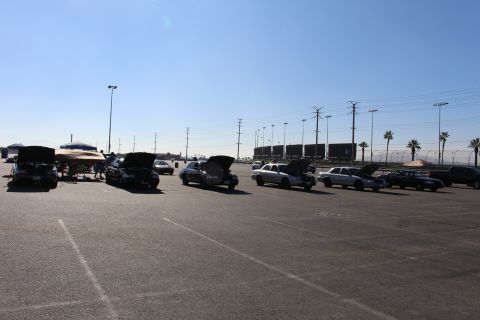 2003 Ford Crown Victoria - line of sedans with their hoods raised sits in a large paved lot under a clear sky, with a boat on a trailer at left.