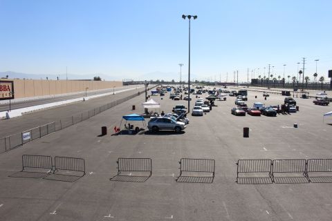 2003 Ford Crown Victoria - wide view of a paved staging lot with scattered cars, pop-up canopies and metal crowd barriers under a hazy sky with mountains behind.