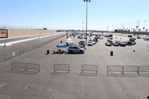 2003 Ford Crown Victoria - elevated view of a paved track lot shows parked cars, a canopy and a silver SUV behind rows of metal crowd barriers.
