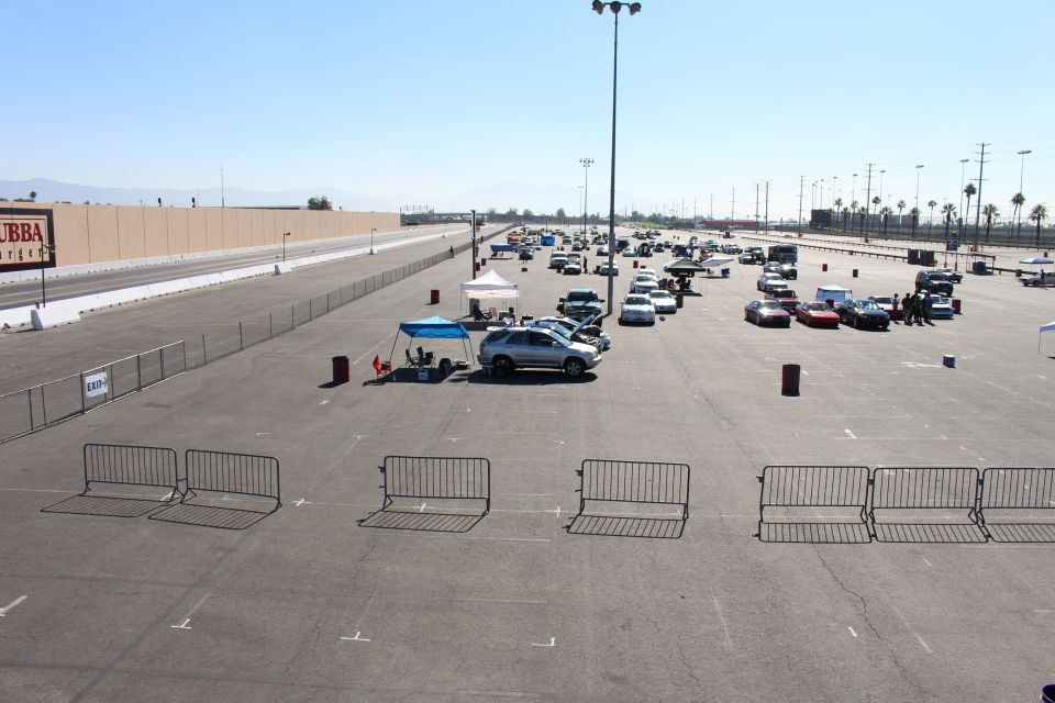 Overview of a track lot with cars, canopy and a silver SUV behind crowd barriers