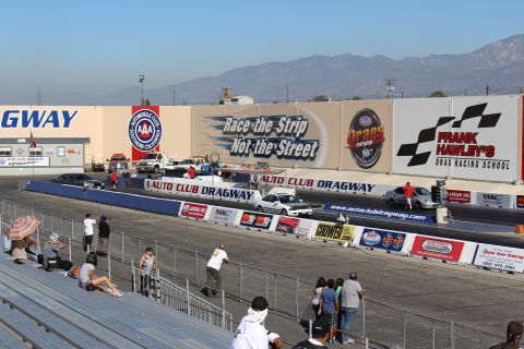 2003 Ford Crown Victoria - Spectators watch from grandstands as cars stage at the Auto Club Dragway start line beneath a "Race the Strip Not the Street" mural.