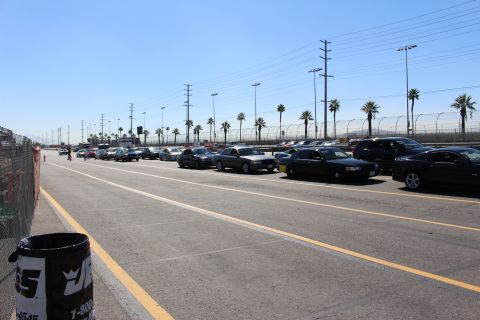 2003 Ford Crown Victoria - row of sedans stages along a yellow-striped lot with palm trees behind and a printed barrel in the foreground.